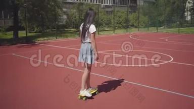 年轻女孩穿着<strong>运动鞋</strong>，裙子和t恤在<strong>户外</strong>篮球场上骑黄色滑板。 影子跟随着